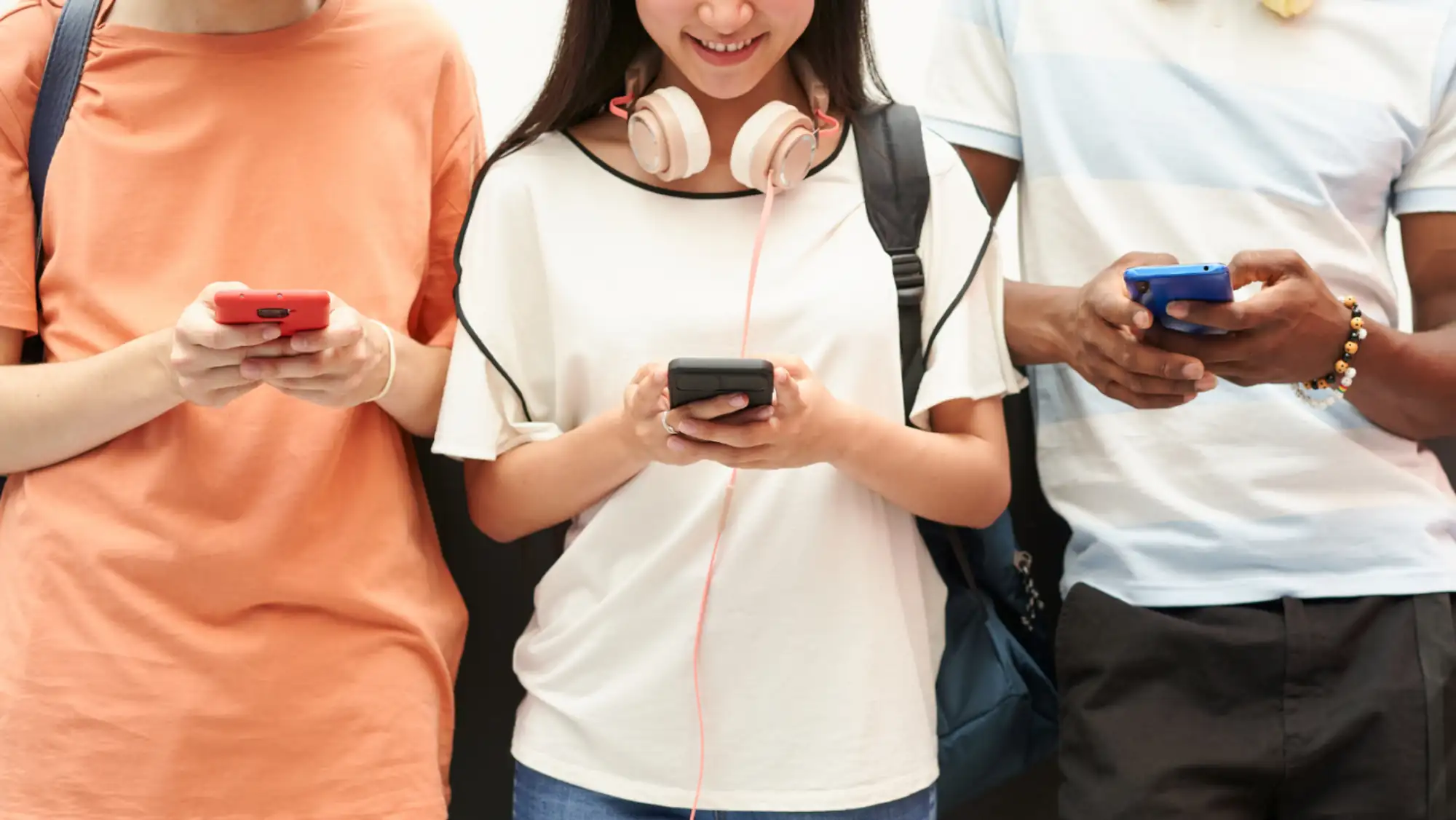 three teens standing side by side, looking at their smartphones