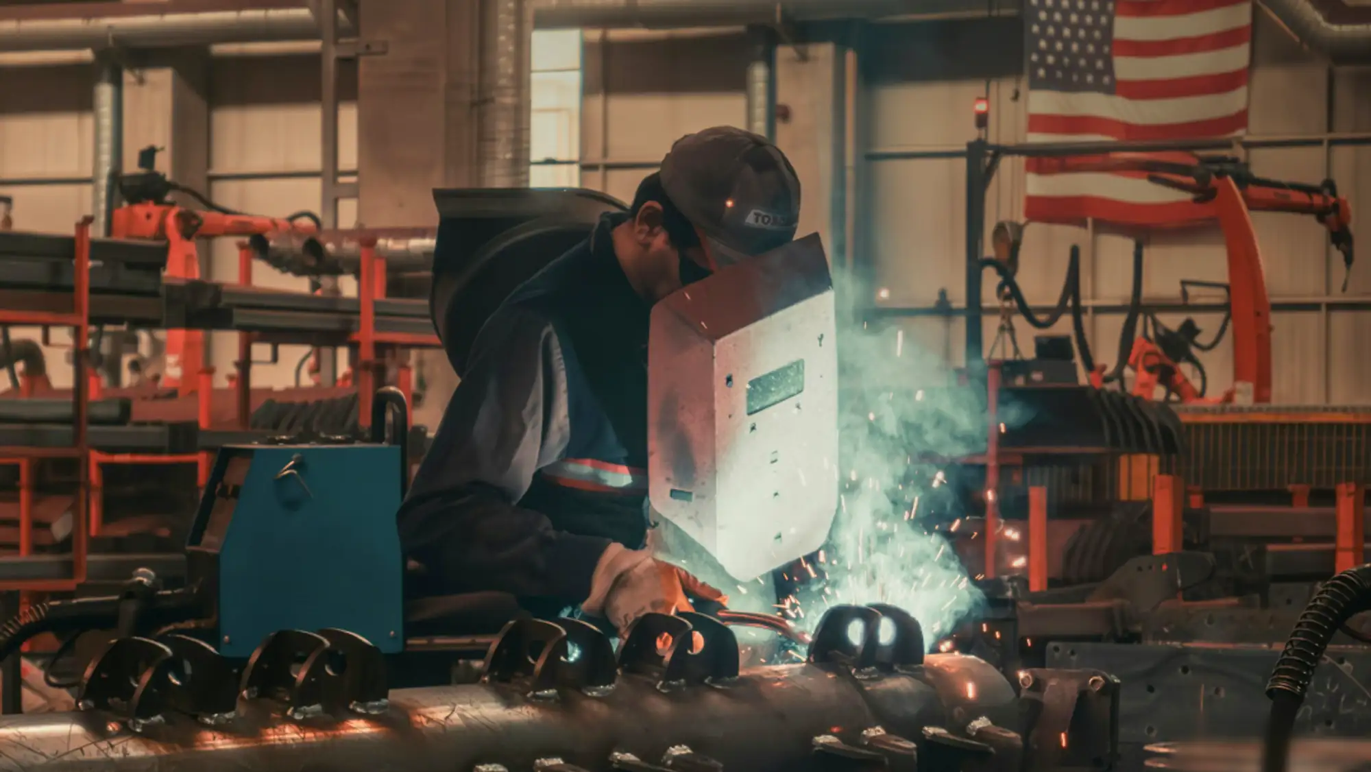A welder working on a shop floor with an american flag in the background to indicate reshoring